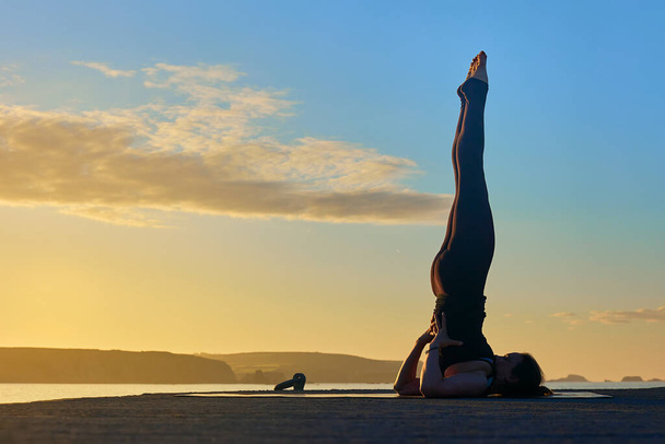 yoga beoefenen buiten het doen van een geavanceerde asana op een pier tijdens een zonsopgang - Foto, afbeelding