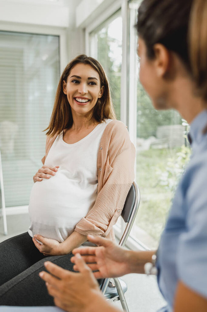 Приваблива вагітна жінка розмовляє з медсестрою під час очікування огляду гінеколога
. - Фото, зображення