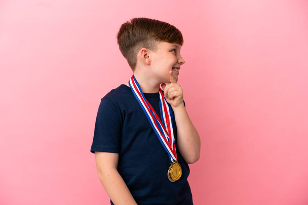 ピンクの背景に孤立したメダルを持つ小さな赤毛の男の子見て側 - 写真・画像