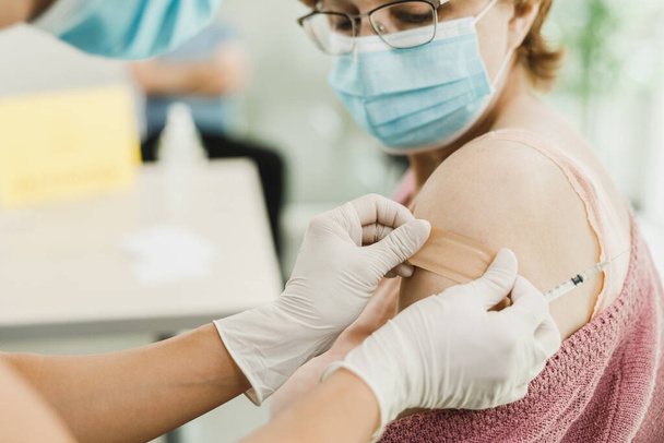 Close-up of a nurse applying a band aid to a senior woman after receiving a vaccine due to coronavirus epidemic. - Photo, Image