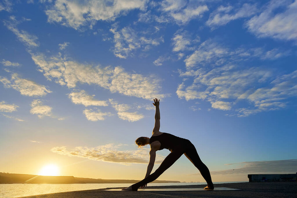 entrenamiento de yoga y meditación en pose en la playa al amanecer o al atardecer. Mujer yoga ejercitando entrenamiento en sereno paisaje oceánico. Silueta como una mujer contra el sol. - Foto, Imagen