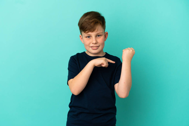 Μικρό κοκκινομάλλικο αγόρι απομονωμένο σε μπλε φόντο κάνει τη χειρονομία του να είναι αργά - Φωτογραφία, εικόνα