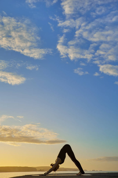 γιόγκα και διαλογισμό σε στάση στην παραλία την αυγή ή το σούρουπο. Γυναίκα γιόγκα άσκηση κατάρτισης σε γαλήνιο τοπίο του ωκεανού. Η Σιλουέτα ως γυναίκα ενάντια στον ήλιο. - Φωτογραφία, εικόνα
