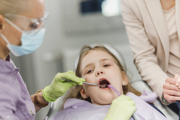 Dentystka badająca zęby uroczej dziewczynki podczas zabiegu stomatologicznego w gabinecie dentystycznym. - Zdjęcie, obraz