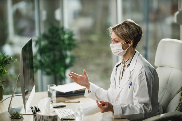 Женщина-врач в защитной маске работает в онлайн-кабинете во время пандемии коронного вируса. - Фото, изображение
