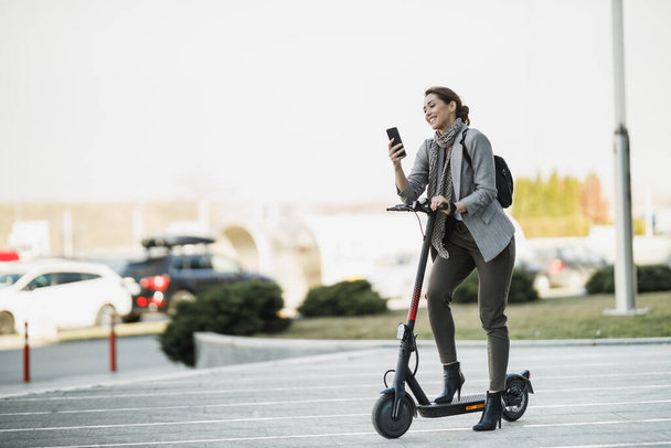 電動スクーターを持つ若いビジネスマンは、彼女のスマートフォンを使用して動作するようになります. - 写真・画像