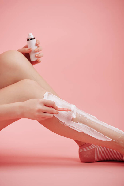 Cropped image of young woman shaving legs with razor blade and foaming cream - Foto, afbeelding