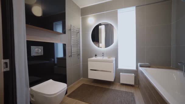 Moderne modieuze residentiële badkamer interieur in nieuw appartement. Een video. Uitzicht binnen in een nieuwe flat na de reparatie, een toilet, een bad, spiegel met verlichting, en een kast met wastafel. - Video