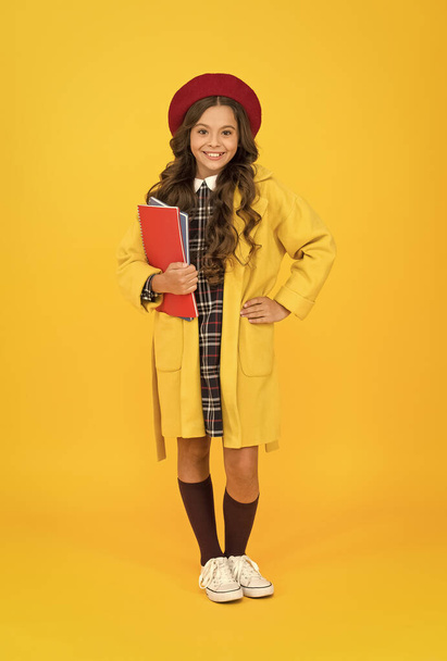 starting study year. stylish teen college student. little girl with notebook or workbook for lesson. education. school and fashion. child in pupil uniform. kid in french beret on yellow background - Photo, image