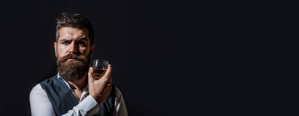 El hombre con barba sostiene brandy de vidrio. Bebida barbuda coñac. Un hombre sosteniendo un vaso de whisky. Bebiendo whisky. Retrato de hombre con barba gruesa. Macho bebiendo - Foto, Imagen