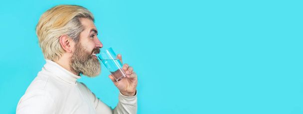 Un uomo barbuto che beve acqua. Uomo barba felice che beve acqua. Un maschio che beve da un bicchiere d'acqua. Concetto sanitario, stile di vita, da vicino. Sorridente maschio tenendo in mano vetro trasparente - Foto, immagini