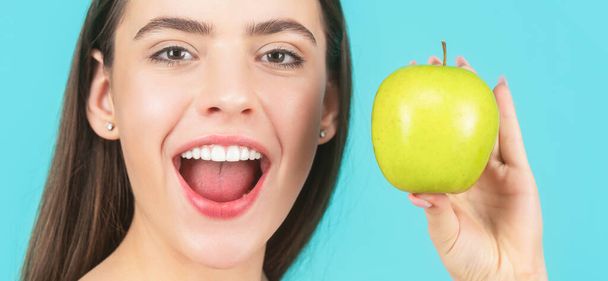 ストーモロジーの概念。完璧な笑顔を保持リンゴ、青の背景を持つ女性。女性は緑のリンゴを食べる。緑のリンゴと若い美しい幸せな笑顔の女性の肖像画。健康的な食事 - 写真・画像