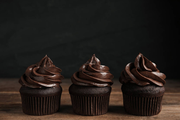 Delicious chocolate cupcakes with cream on wooden table against dark background. Space for text - Φωτογραφία, εικόνα