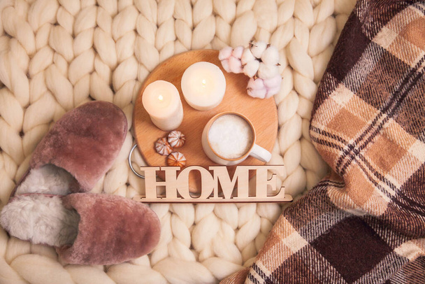 Huisbontpantoffels. kopje cappuccino en koekjes, geruite plaid, inscriptie Thuis op de deken van dikke garen met kopieerruimte. De sfeer van huiselijkheid en comfort. - Foto, afbeelding