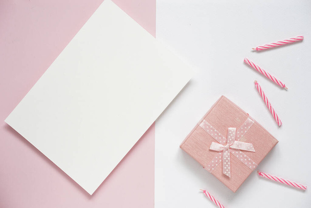 üdvözlőlap születésnapi vagy ünnepi szezonális ötletek top view üres fehér brosúra mock up elhelyezett rózsaszín pasztell papír és fehér papír háttér ellen rózsaszín ajándék doboz és rózsaszín születésnapi gyertyák, másolás hely. - Fotó, kép