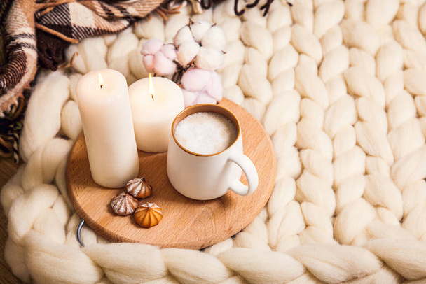 Šálek cappuccino a sušenky, svíčky, kostkované kostkované na pozadí přikrývky z tlusté příze. Atmosféra domácnosti a pohodlí. - Fotografie, Obrázek