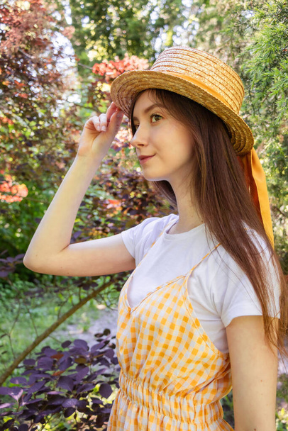 Profile photo of a brunette girl in a wicker straw hat with a ribbon in the park - Photo, Image