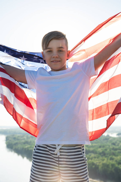 Blondynka machająca narodową flagą USA na zewnątrz nad błękitnym niebem nad brzegiem rzeki - Zdjęcie, obraz