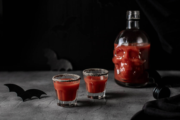 Tomatencocktail in een schedelvormige fles en glazen. Drink voor Halloween feest op donkere achtergrond - Foto, afbeelding