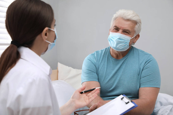 Doctor examining senior man with protective mask at nursing home - Фото, зображення