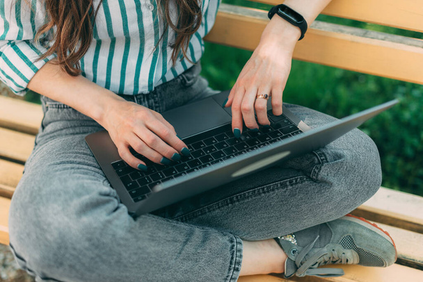 Photo of woman sits on the wooden bench and working on laptop computer outside - 写真・画像