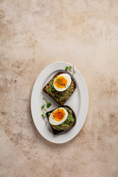 Healthy sandwich with avocado, eggs and microgreens on toast on a serving plate for breakfast. Healthy nutrition dietary concept. Top view - Foto, afbeelding