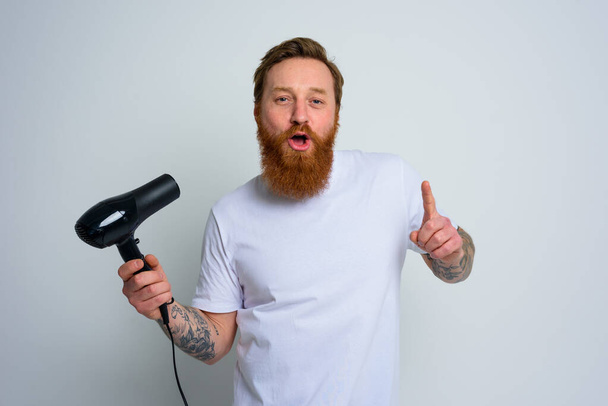 Glücklicher Mann mit Bart nutzt Föhn als Mikrofon und tanzt - Foto, Bild