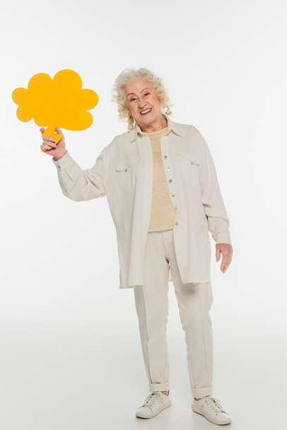 smiling elderly woman in casual clothes holding yellow thought bubble in hand on white - 写真・画像