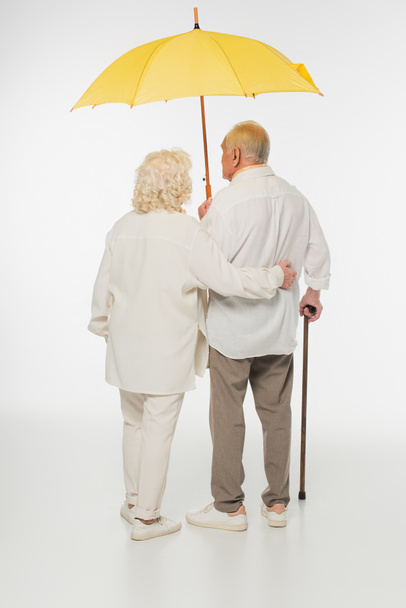 visszapillantás idős pár alkalmi ruhák séta sárga esernyő és ragad a fehér - Fotó, kép