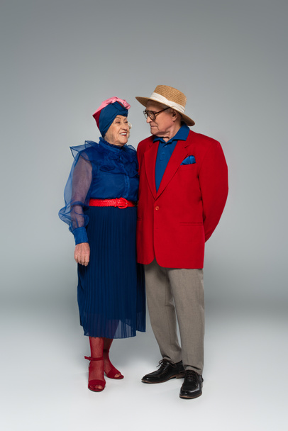 sonriente pareja de ancianos en ropa elegante de pie en gris - Foto, imagen