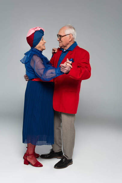 feliz pareja de ancianos en ropa elegante bailando en gris - Foto, imagen