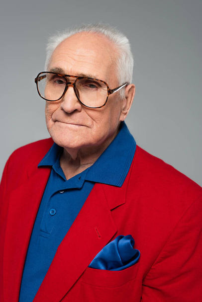 portrait of serious elderly man in red blazer and glasses isolated on grey - Zdjęcie, obraz