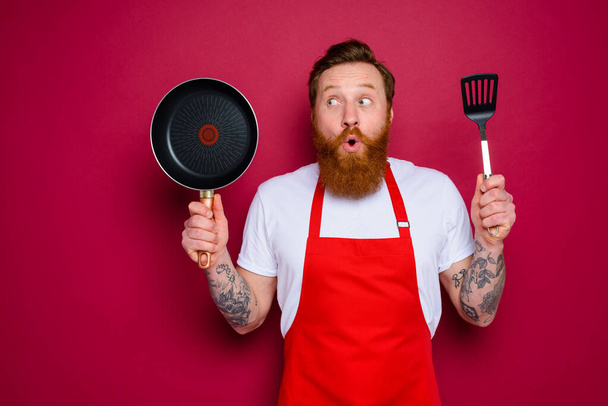 überraschter Koch mit Bart und roter Schürze ist bereit zum Kochen - Foto, Bild