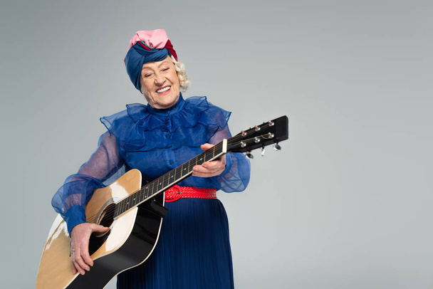 donna anziana sorridente in abiti alla moda con chitarra acustica isolata su grigio - Foto, immagini