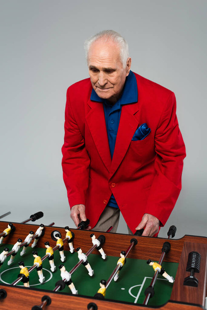 Senior im roten Blazer beim Tischkicker auf grau - Foto, Bild