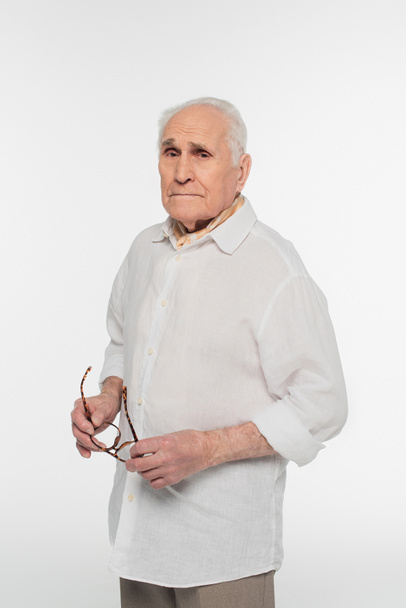 smiling elderly man in casual clothes holding glasses in hands isolated on white - Foto, Imagem