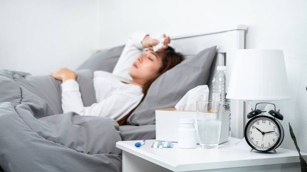 Asian woman feeling sick and sleeping in blanket on the bed while holding tissue in hand and touching forehead after using thermometer to checking body temperature and take medicine in bedroom at home - Foto, Imagem