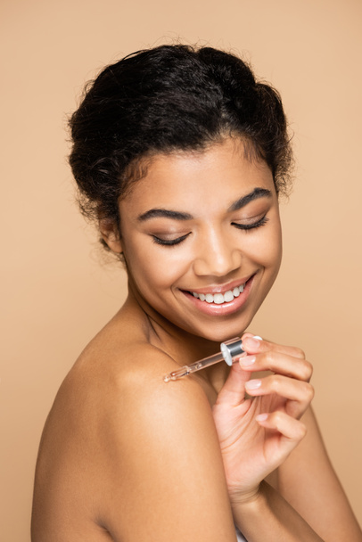 boldog afro-amerikai nő csupasz vállak alkalmazó szérum csupasz váll izolált bézs  - Fotó, kép