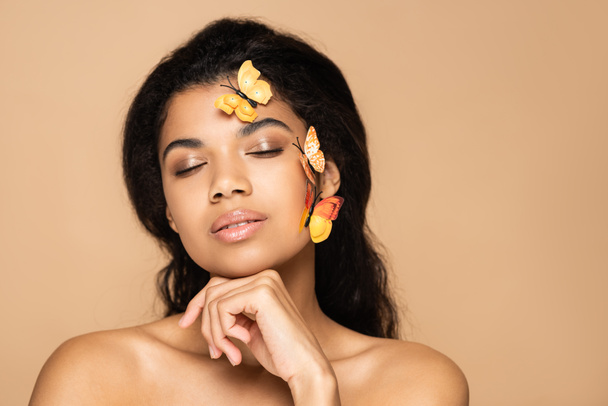 jeune femme afro-américaine avec des papillons décoratifs sur la joue isolé sur beige - Photo, image