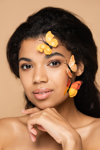 young african american woman with butterflies on face looking at camera isolated on beige - Фото, зображення