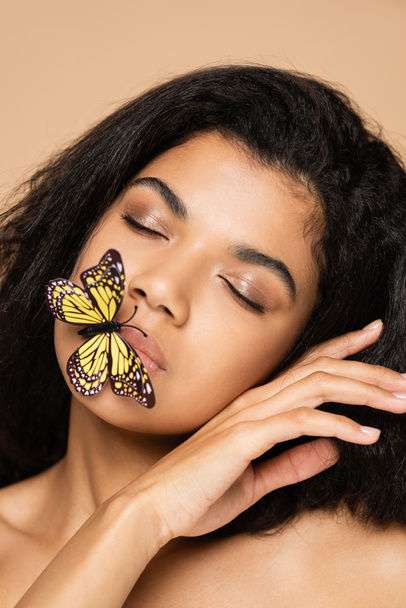 young african american young woman with closed eyes and butterfly on lips isolated on beige  - Foto, Imagem