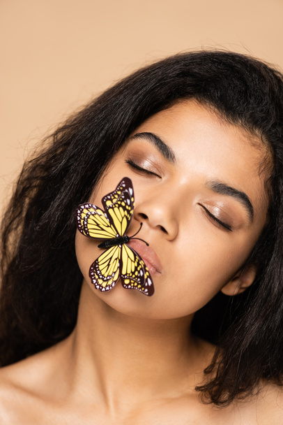 african american young woman with closed eyes and butterfly on lips isolated on beige  - Photo, Image
