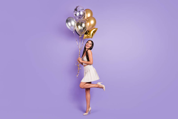 Full size profile side photo of charming happy woman hold golden balloons smile isolated on purple color background - Valokuva, kuva
