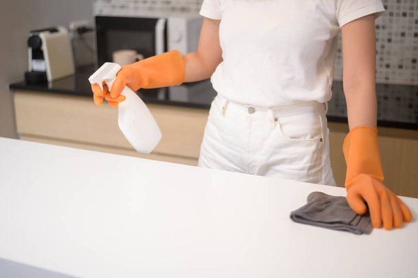 A young beautiful woman wearing protective rubber gloves is cleaning table in kitchen at home. - Foto, Imagen