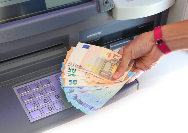 main avec de nombreux billets en euros juste ramassés au guichet automatique et le clavier numérique pour entrer le code PIN - Photo, image