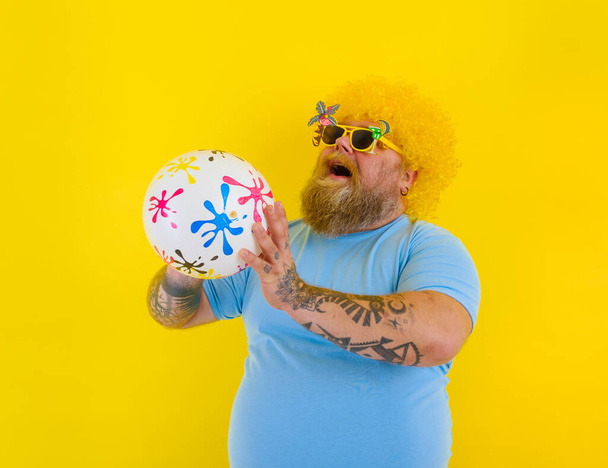 Grasso uomo con parrucca in testa e occhiali da sole divertirsi con una palla - Foto, immagini