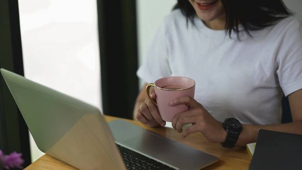 Colpo ritagliato womanworking sul computer portatile mentre beve caffè in ufficio. - Foto, immagini