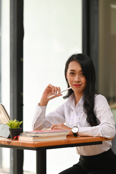 Young asian woman looking at camera and sitting on office workplace. - Fotó, kép