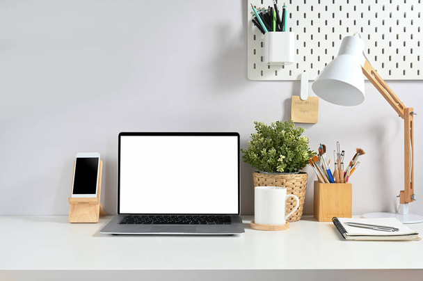 Comfortabele werkruimte wordt omringd door een witte scherm laptop en diverse apparatuur. - Foto, afbeelding
