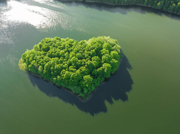 Θέα από το drone στο νησί σχηματίζεται με τη μορφή μιας πράσινης καρδιάς που περιβάλλεται από νερό, μια λίμνη. Όμορφο τοπίο με ένα drone σε μια ενδιαφέρουσα λίμνη - Φωτογραφία, εικόνα